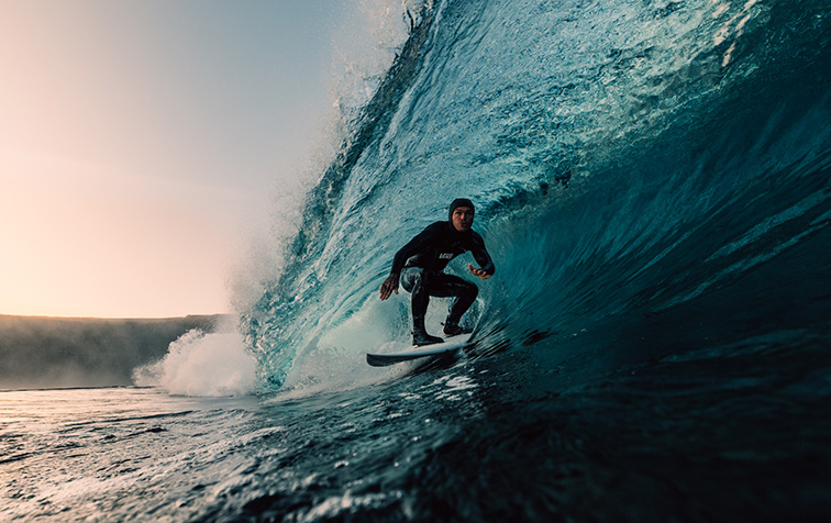 Film still for Let Me Live - A surfer rides inside the barrel of a large wave during golden hour lighting.