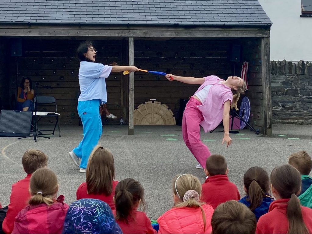 Two dancers perform a contemporary routine in front of a group of students in a school pplayground