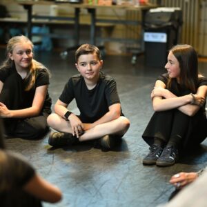 3 young people sit on rehearsal room floor
