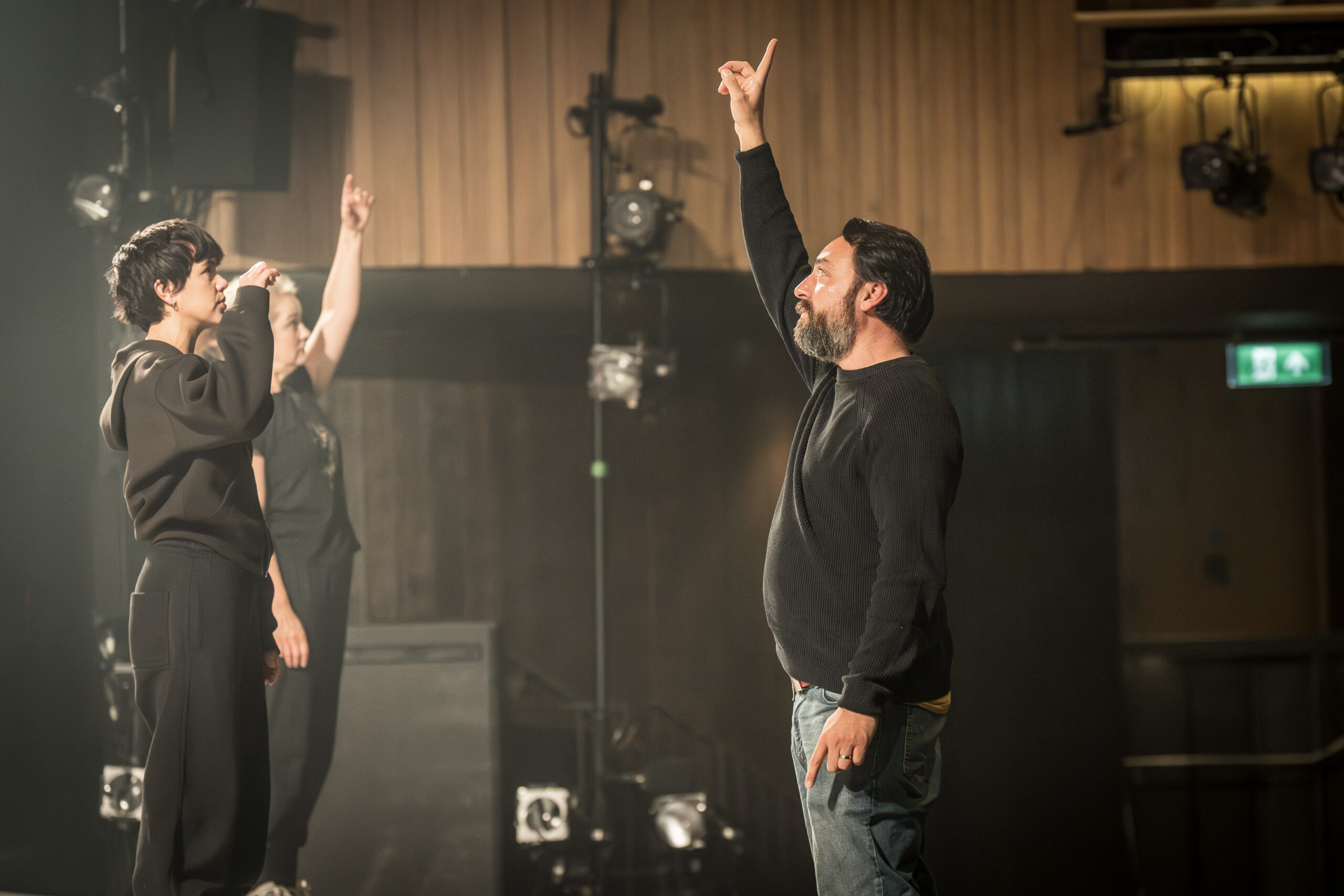 A man with black hair and beard raises arm in the air as if indicating music pitch