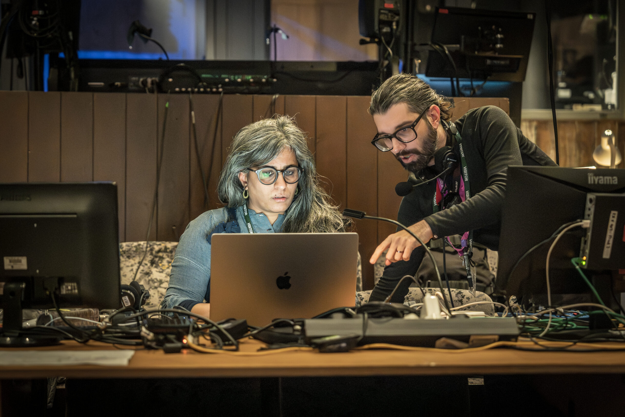 One woman and one man, both wearing glasses, pore over a computer screen