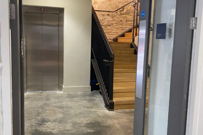 A photo of 2 opened grey double doors, revealing a lift on the lefthand side, and a set of stairs on the right. 