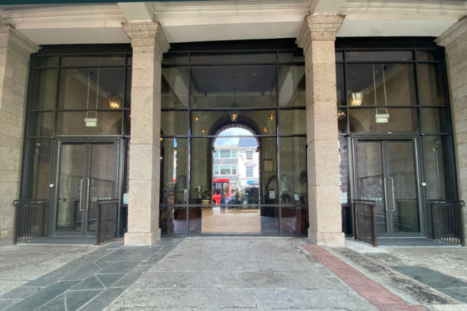 A photo of the Hall for Cornwall building from Boscawen Street, showing 2 stone pillars over a marbled floor. The wall behind is entirely glass, with two automatic doors either side. 