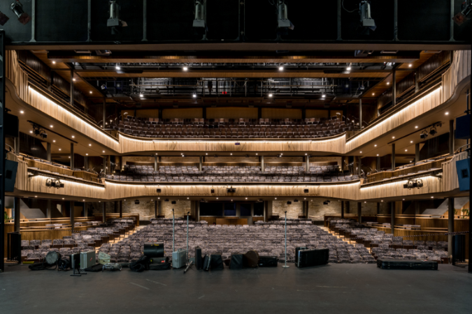 A photo of the Cornwall Playhouse auditorium, taken from the stage. The seats are empty, and you can see up to the balcony level. 