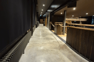 A photograph of the “opeway” that runs along the back of the Cornwall Playhouse auditorium on the stalls level. It is a long flat corridor, running along the back wall, behind the sound booth and seating. 