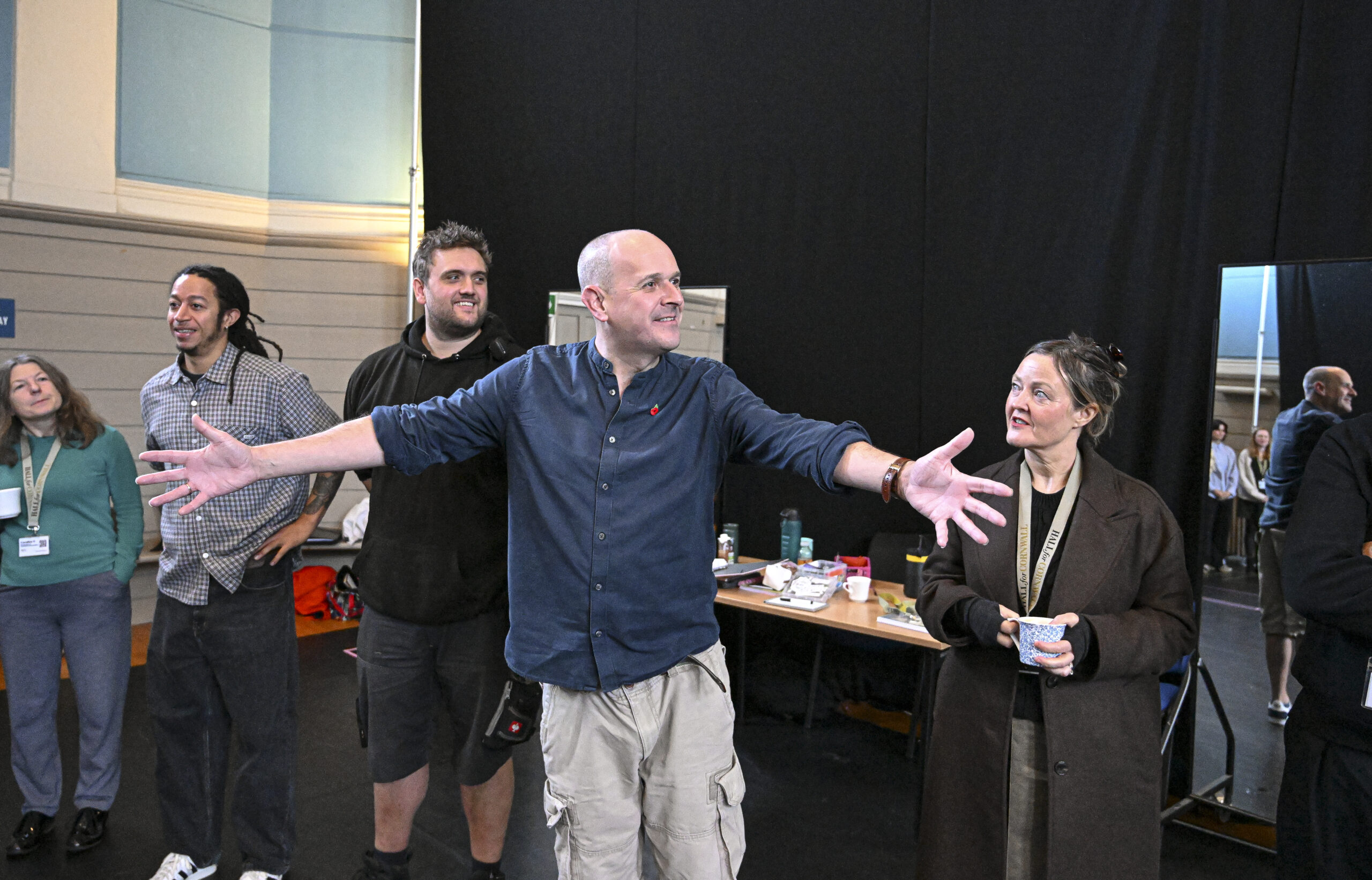 Director Nick Evans holds his arms wide as he talks to a group of people in the rehearsal room.