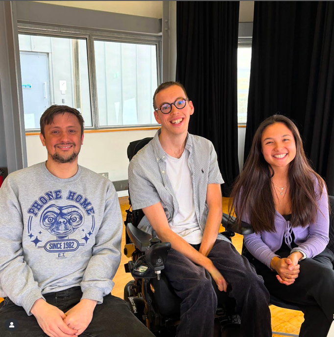 3 creatives sit smiling at the camera. Alex is on the left, wearing a grey jumper. He is a white man with short brown hair and a brown beard. Keron is in the middle. He is a white male wheelchair user with short brown hair and glasses. He wears a grey shirt. Helen is on the right. She is an asian woman and has long dark hair. She is wearing a grey/purple cardigan.